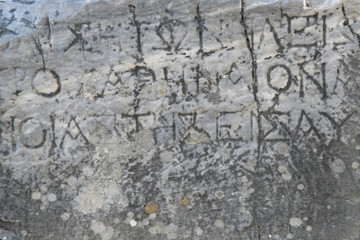 Half-erased ancient Greek letters embossed on an old gray marble slab covered with cracks and mold.
