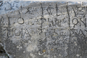 Half-erased ancient Greek letters embossed on an old gray marble slab covered with cracks and mold.