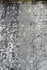 Half-erased ancient Greek letters embossed on an old gray marble slab covered with cracks and mold.