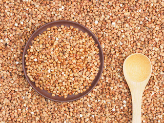 Clay plate with buckwheat groats and bamboo spoon on buckwheat background. Healthy eating concept