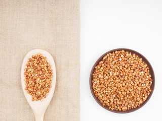 Buckwheat groats in clay plate and in wooden spoon on gray fabric and white background. Weight loss concept