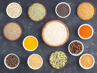 Rice, allspice, pepper chili, fenugreek, cloves, turmeric, masala, dry ginger, fennel, green cardamom, mustard seeds in bowls on black concrete background with copy space. Indian cuisine concept