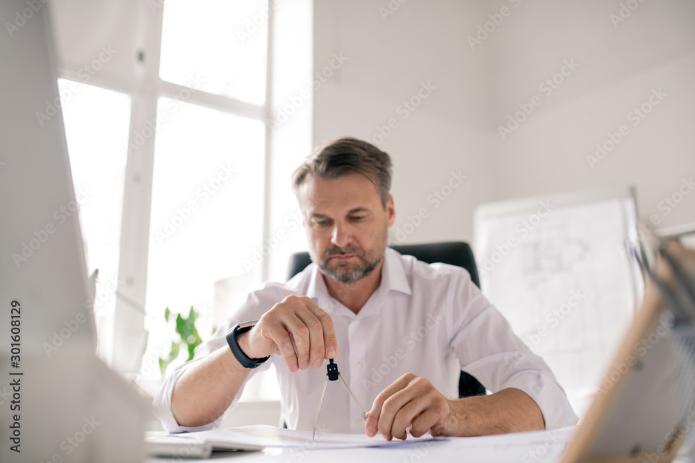 Poster mature bearded engineer in white shirt using dividers while working over sketch