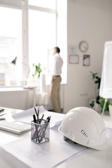 Workplace of modern architect with white hardhat, bunch of pencils and sketches