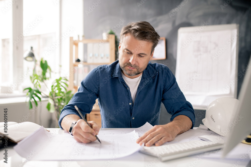 Poster serious mature architect drawing new sketch on paper while sitting by desk
