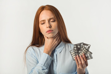 beautiful young woman with red hair with pills in hands on a white background