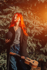 Fototapeta premium Sexy redhead girl with long hair plays the ukulele. Perfect woman portrait. Gorgeous strong and thick hair. Deep blue eyes. Natural beauty, clean skin, face and hair care.