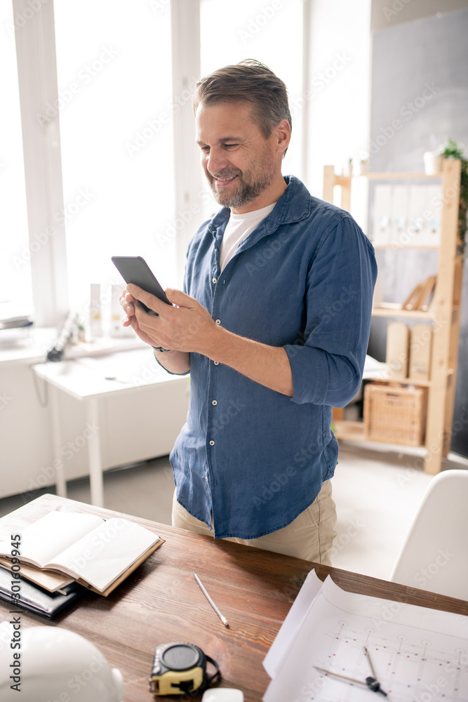 Aufkleber cheerful mature engineer with smartphone scrolling through contacts or texting