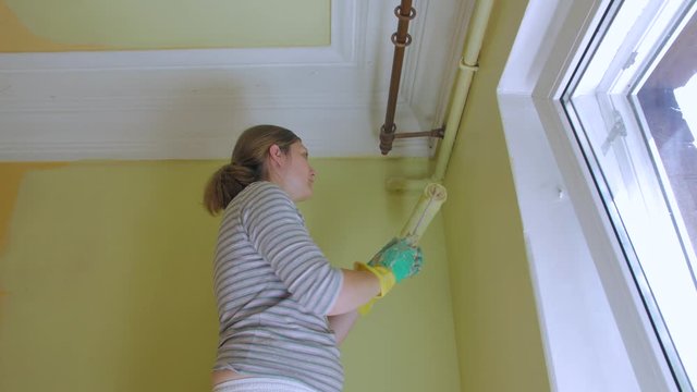 Young woman paints the walls in yellow lemon color in house indoors apartment interior repair