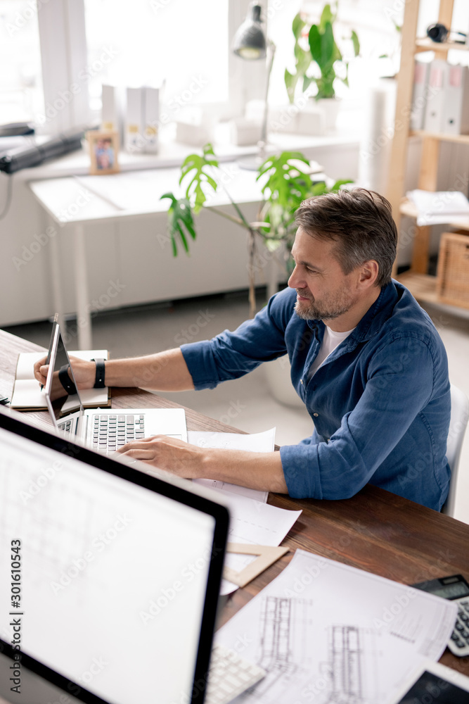 Poster Serious engineer looking at data on laptop display while surfing in the net