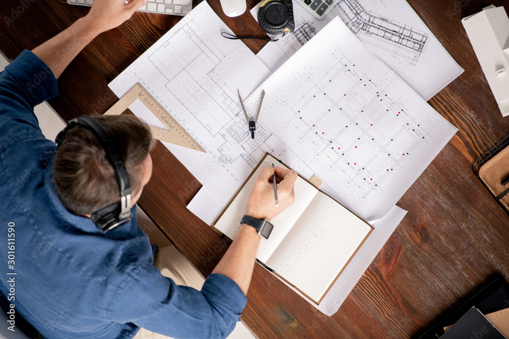 Poster Top view of professional engineer with notebook and pencil making working notes