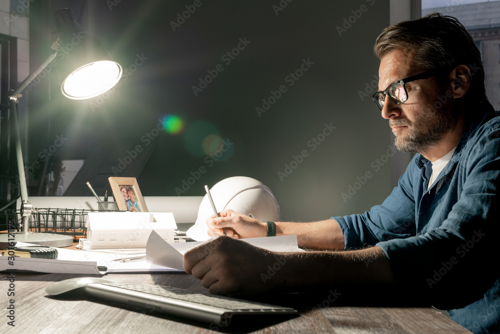 Poster serious architect working over new project in office late in the evening