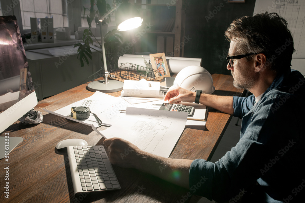 Poster contemporary engineer working with sketches while staying in office late