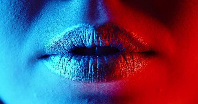 Close up shot of lips of a young girl with glowing makeup making a beautiful positive sensual smile in neon light - emotions, nightlife concept 4k footage