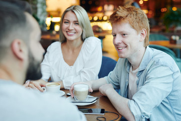 Happy guy with cup of cappuccino and his girlfriend talking to their friend