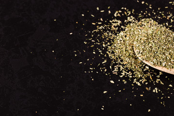 Crushed oregano scattered in a wooden spoon on a black table. Concept, copy space.