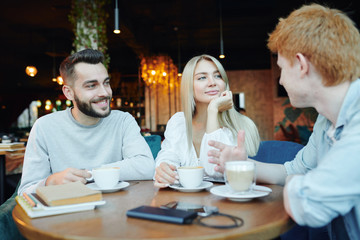Happy young heterosexual couple chatting to their friend by cup of cappuccino