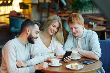 Pretty blonde girl and two happy guys scrolling through photos in smartphone