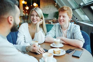 Happy young casual couple chatting to their friend by cup of coffee and dessert