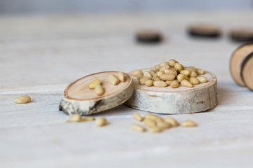 On a wooden table lies a small round board of birch and dark wood, on which peeled pine nuts are poured closeup.