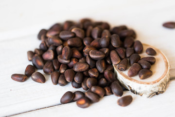 On a white table and a round board made of birch are brown unpeeled pine nuts in a close-up.