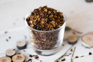 A brown shell from a pine nut with a blurry white wood background is poured in a transparent glass...