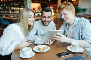 Cheerful man showing his friends curious video in tablet while relaxing in cafe