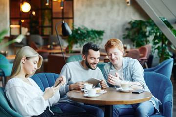 Fototapeta premium Two guys with gadgets watching video and pretty girl scrolling in smartphone