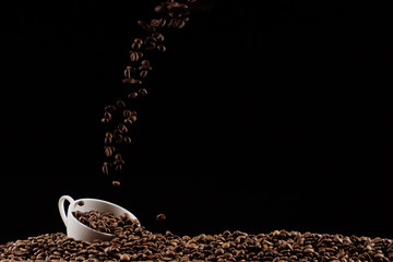 Naklejka premium A cup with coffee beans in the air flying in flight like a spray. On a black background, coffee shop advertising concept, copy space.