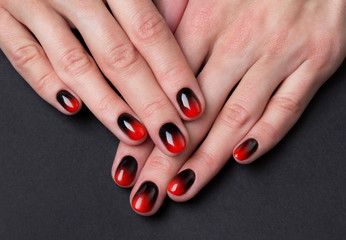 Two female hands with red black ombre gradient nails on dark background © Darya Lavinskaya
