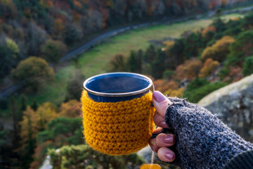 Woman hand wearing knitted fingerless gloves holding a cozy crochet mug with hot tea on a cold...