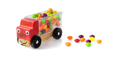 multi-colored candies fell from the back of a red children's toy car. Candy boom. White background.