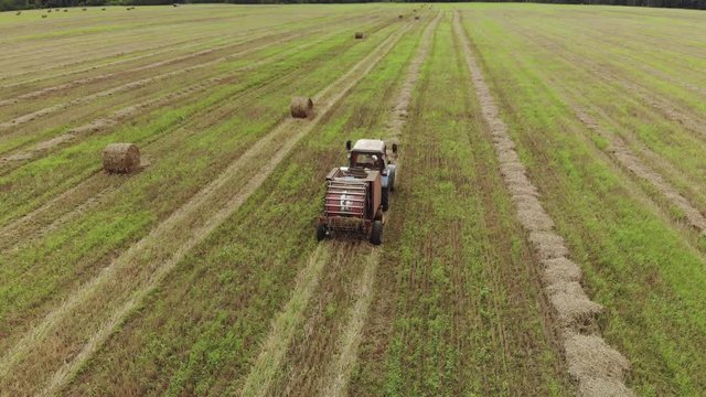 Aerial view of a tractor producing straw pressing on a harvested agricultural field. From the trailer baler comes ready roll