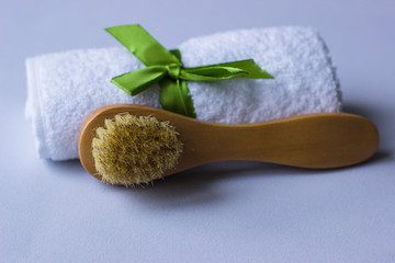 Wooden soft massage brush for body and towel with green ribbon on grey background, copy space. Skin care products. Massage brush with natural bristles for body peeling or anti-cellulite massage. 
