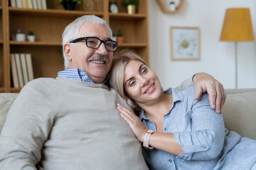 Young smiling woman putting head on shoulder of her senior father embracing her