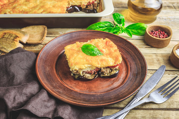 Delicious meat casserole with eggplant, minced meat, tomato, bechamel sauce and cheese. Greek moussaka on rustic wooden background. Selective focus