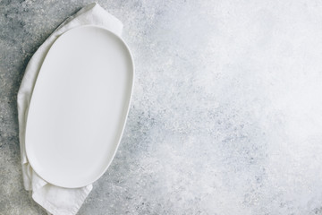 Empty white oval plate and white napkin on light gray background table. Top view. Copy space. Flat lay. Minimal concept