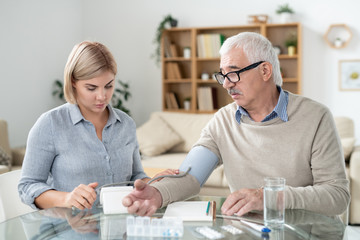 Fototapeta premium Careful daughter taking care of her sick retired father while using tonometer