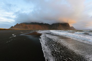 Magical landscape of Vestrahorn Mountains and Black sand dunes in Iceland at sunrise.  Panoramic view of the Stokksnes headland in a Colorful seascape.