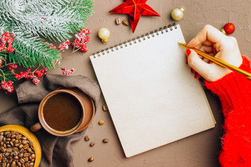 Naklejka na ściany i meble Christmas composition: notebook, pen, coffee cup and beans, fir branch on brown background. Woman's hand holding cup of coffee and writing 2020 Goals or plans in craft notebook. Flat lay, top view