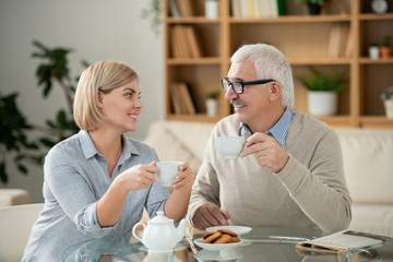 Cheerful young woman and her elderly father with tea looking at each other