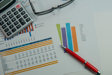 Selective focus of chart graph document with eye glasses, calculator and pen on top. Showing report by monthly with statistic graph.