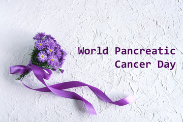  World Pancreatic Cancer Day text on white textured background with purple flowers and purple ribbon. Flat lay, top view.           