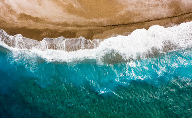 Fototapeta na wymiar waves of the turquoise sea with blue layers from the sandy shores, texture view from above with drone