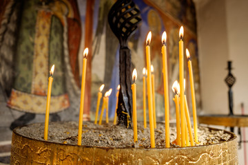 Lighted church wax candles in the sand stand. Burning group of candles in church. Close-up. Selective focus.