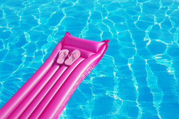 Beach summer holiday background. Inflatable air mattress, flip flops on swimming pool.