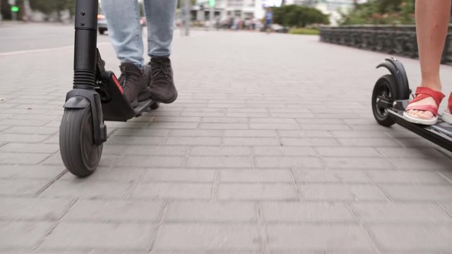 guy legs in black snickers ride future technology electric scooter with girlfriend on pavement close low angle arc shot