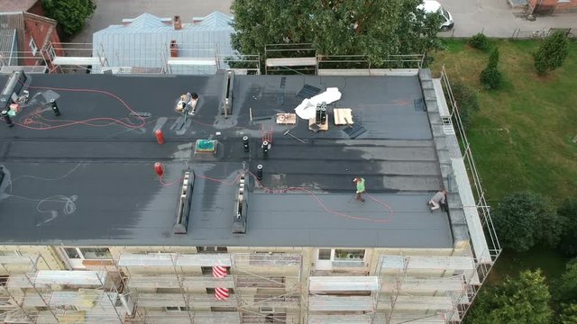 Workers roofers repair flat house roof in city, aerial view