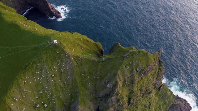 Aerial drone video flying over Kallur lighthouse on green hills of Kalsoy island, Faroe islands, Denmark. UHD 4k video