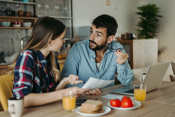 Young couple arguing while having problems with their home finances at dining table